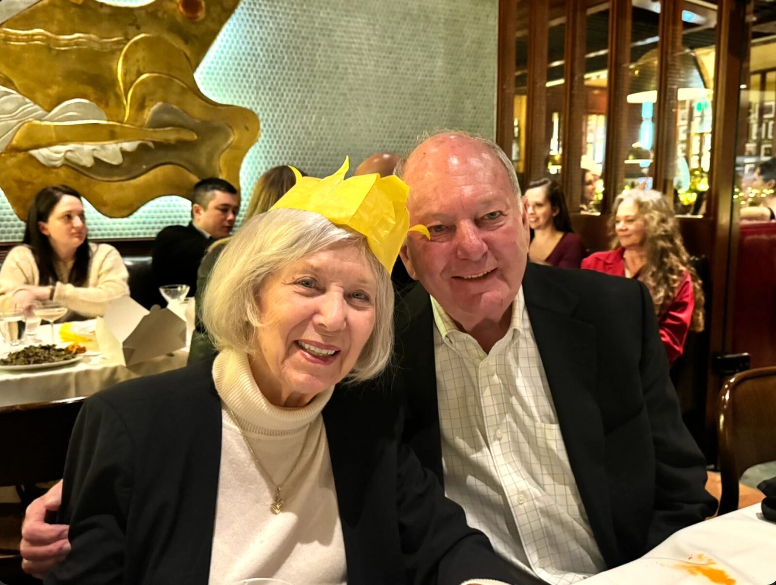 Jan wearing a yellow paper crown and Jim with his arm around her, both smiling at a table in Original Joe's in San Francisco